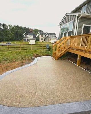 Exposed aggregate concrete patio with a curved gray border beside a wood deck in Huntersville, NC
